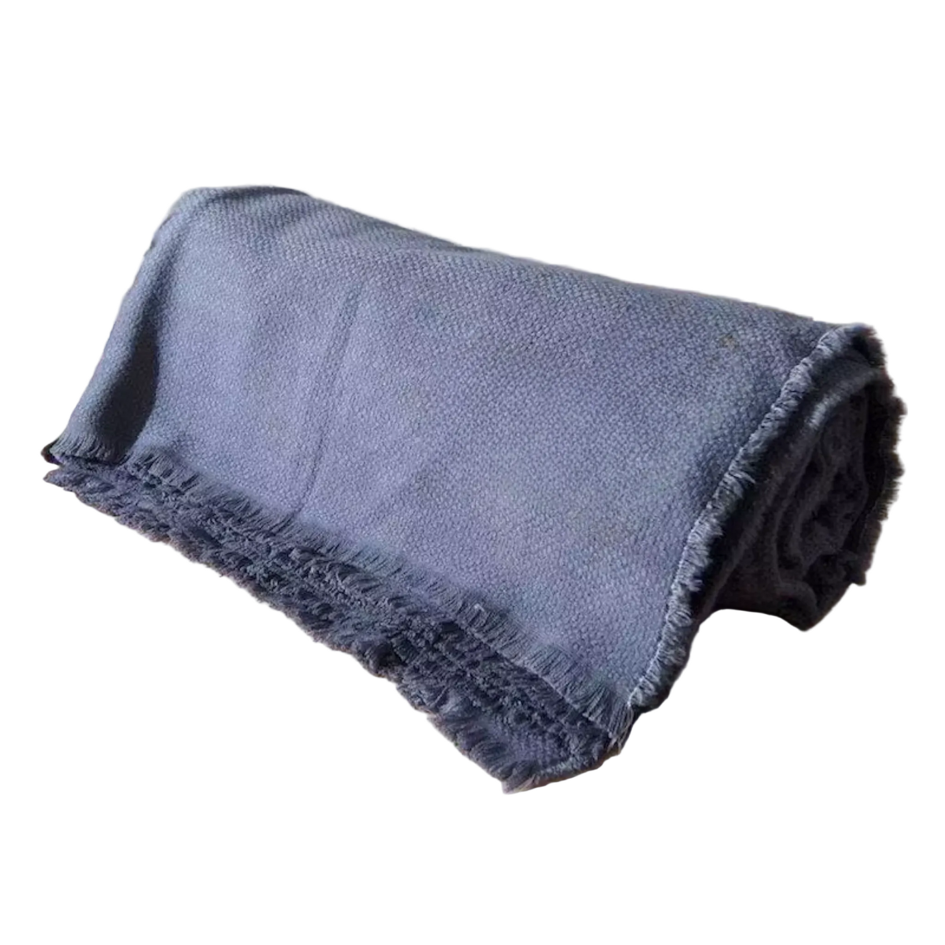  Slate Blue cotton throw blanket rolled and resting on a wooden surface with dried botanicals beside it, highlighting the textured waffle weave and soft fringe trim detail