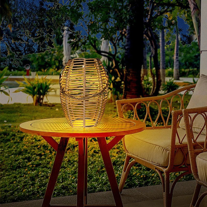  Rattan solar lantern glowing with warm amber light on a wooden side table on a covered patio, styled with a rattan armchair and lush tropical garden in the background