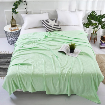 "Aqua Weave" 100% bamboo fibre cooling summer blanket in Sage Mint draped over a bed in a bright natural bedroom with monstera plant and rattan accents