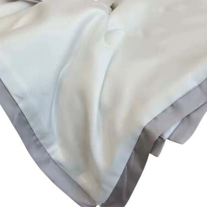  Close-up of the Ivory White eucalyptus lyocell cooling quilt showing the silky-smooth fabric drape and soft grey satin border trim detail against a white background