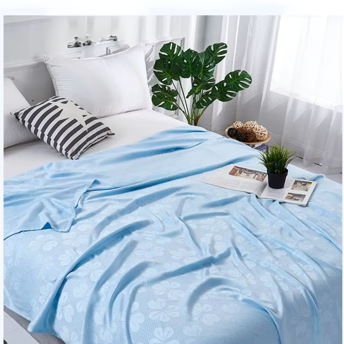 "Aqua Weave" 100% bamboo fibre cooling summer blanket in Sky Blue draped over a bed in a bright Scandinavian-inspired bedroom with monstera plant