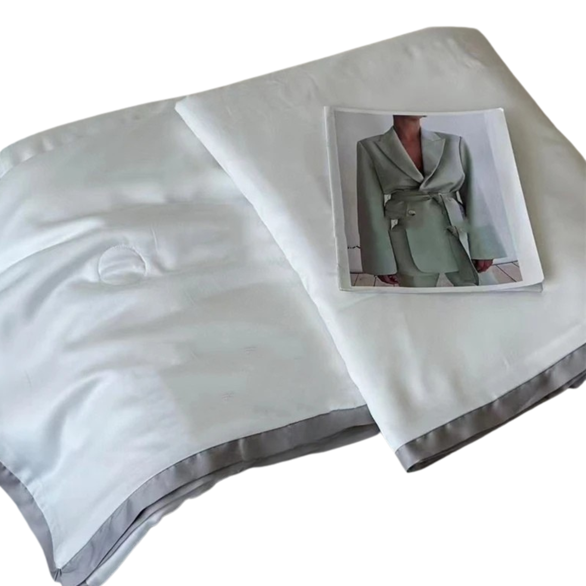  Ivory White eucalyptus lyocell cooling quilt folded and displayed against a white background with a fashion editorial print as a styling prop, showing the silky-smooth fabric and soft grey satin border trim