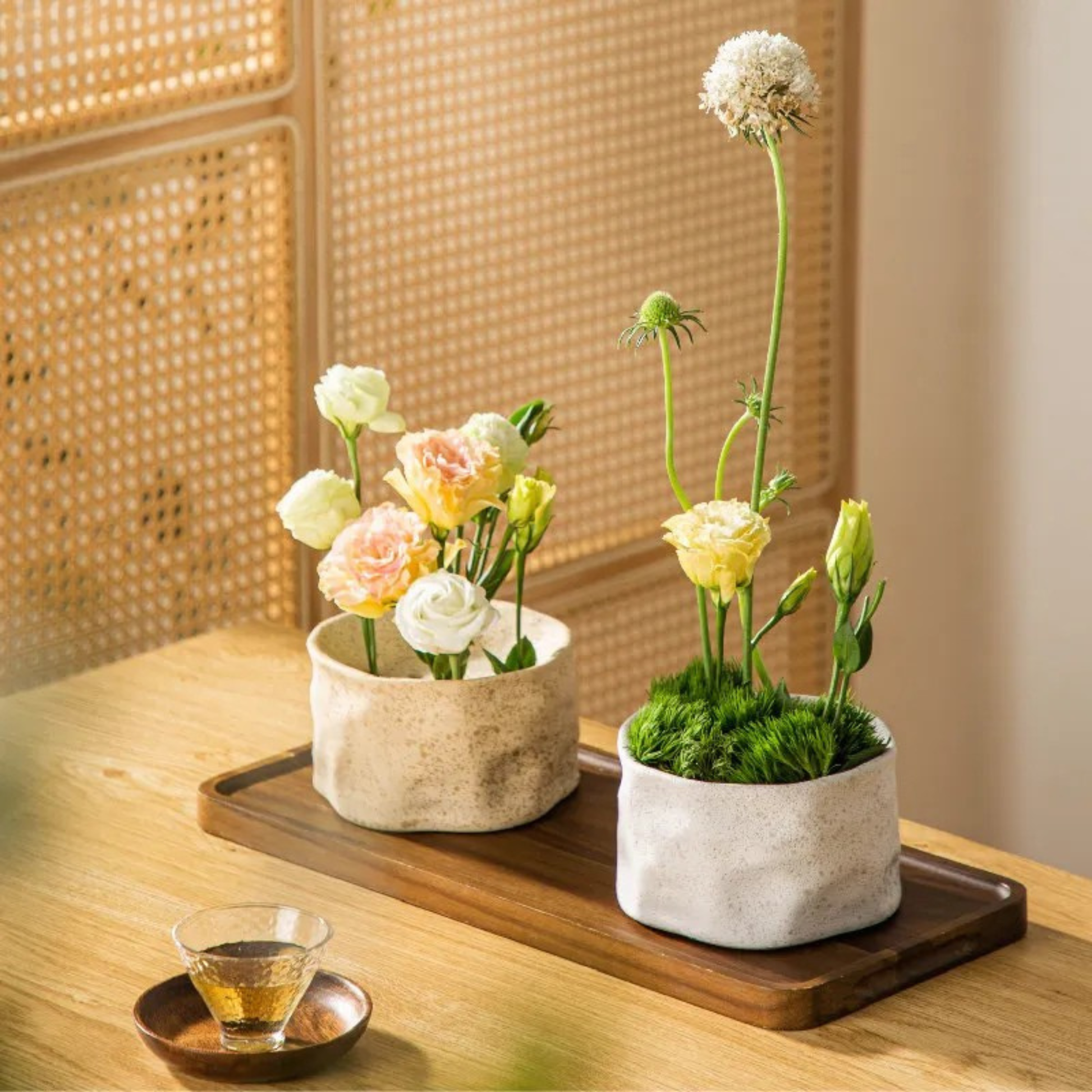 "Stone and White kenzan ceramic ikebana bowls on wooden tray with pastel flower arrangements and tea glass"