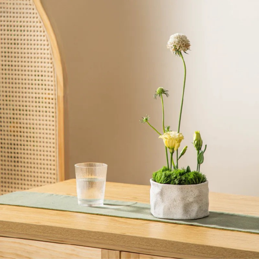 Sand wabi-sabi kenzan bowl with dried flower arrangement on wooden surface"