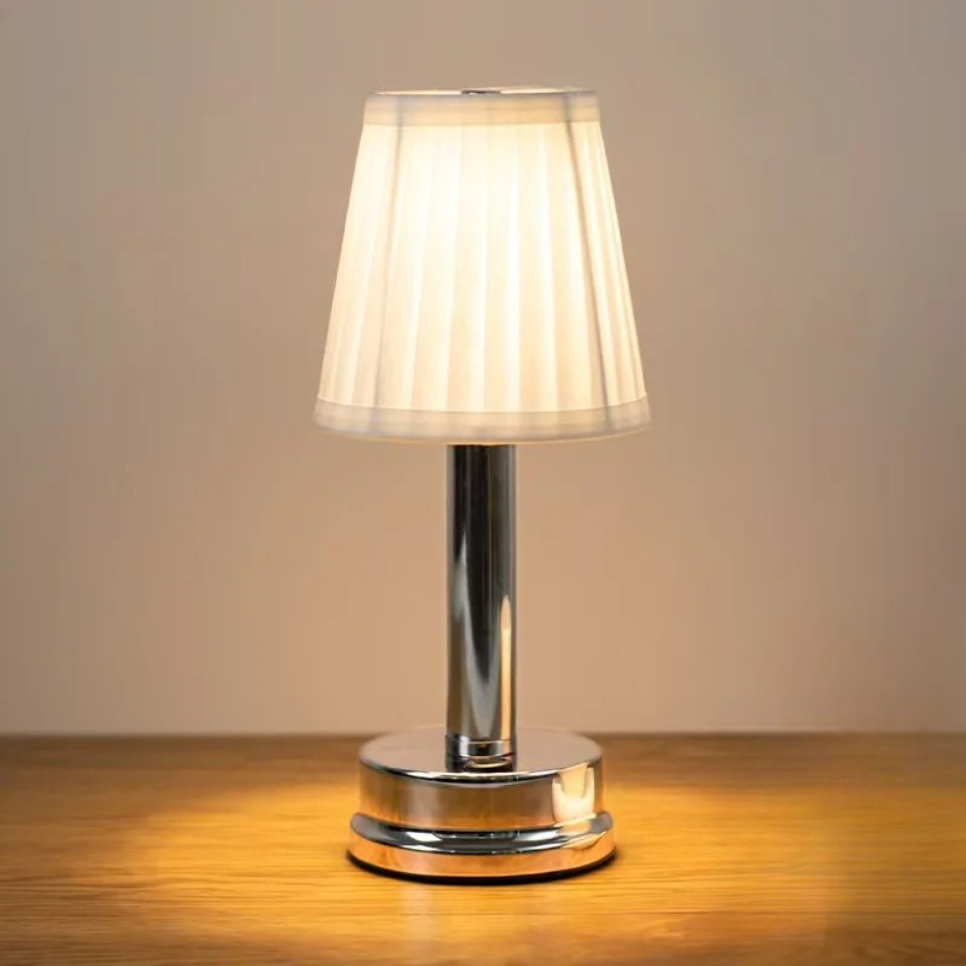  Silver rechargeable touch table lamp with pleated fabric shade glowing warm white on a wooden surface, against a neutral beige background