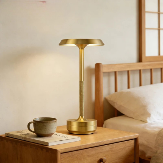  Gold disc-shade rechargeable table lamp glowing with warm light on a wooden bedside table, styled with a ceramic cup and book — "Disc & Stem" by CL House