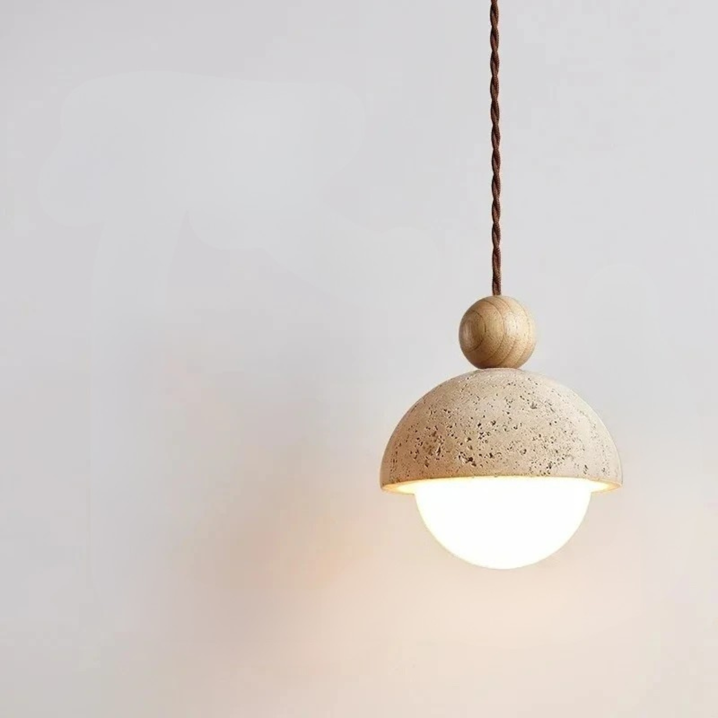  Stone & Orb travertine pendant light with textured cream stone dome, frosted glass globe and log wood bead glowing warm light against a soft white wall