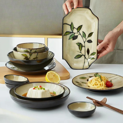 "Painted Leaf" ceramic tableware collection styled on a dining table, including soup bowls, dinner plate with pasta, rectangular serving tray held by hand, hand-painted leaf motif in ivory and espresso glaze, japandi dining setting