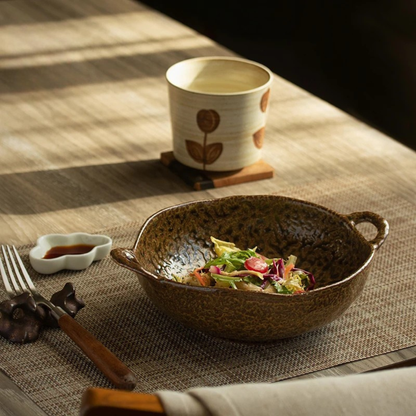 "Wabi Crest" stoneware serving bowl in earth brown with fresh salad — lifestyle shot on linen table runner with ceramic cup, flower-shaped sauce dish and wooden cutlery in warm natural light