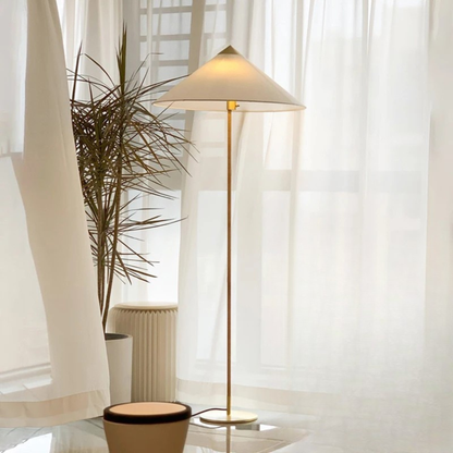"Cone & Brass" floor lamp with linen shade beside a tall plant and sheer white curtains in a bright living room