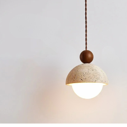  Stone & Orb travertine pendant light with textured cream stone dome, frosted glass globe and walnut wood bead glowing warm light against a soft grey wall