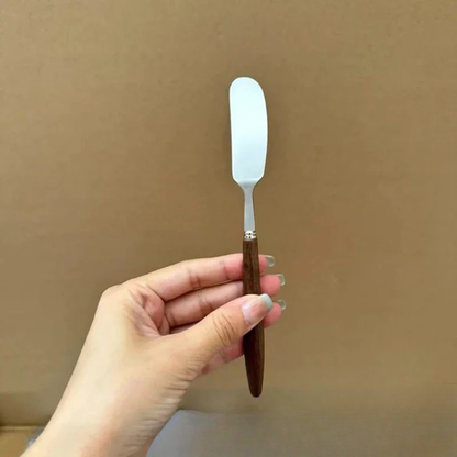  Hand holding "Walnut Stem" butter knife vertically — showing the stainless steel spreader blade and dark walnut handle — scale reference shot