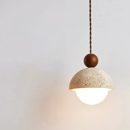Stone & Orb travertine pendant light with textured cream stone dome, frosted glass globe and walnut wood bead glowing warm light against a soft white wall, side angle view
