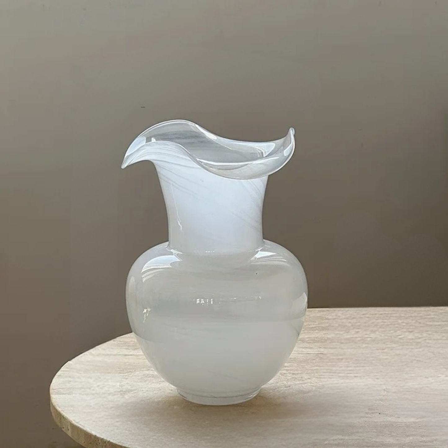 "Petal Wave" handblown glass vase in Milk Swirl — round body with asymmetric wave rim, white swirl glass, styled on wooden side table with neutral background